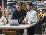 Two men and a woman stood up looking at a laptop